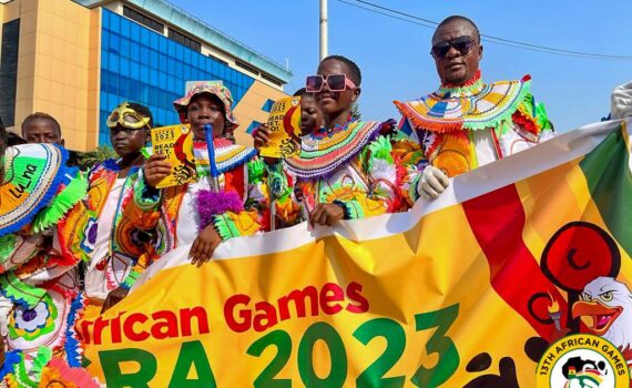 13th African Games parade with people dressed in colorful clothes holding a banner.